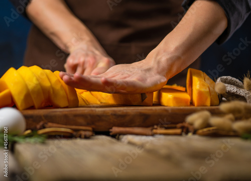 The chef prepares the filling for the American pumpkin pie. She cuts the pumpkin into slices on a cutting board. Wooden texture. Family Birthday Cake For Thanksgiving, Halloween, Christmas, New Years