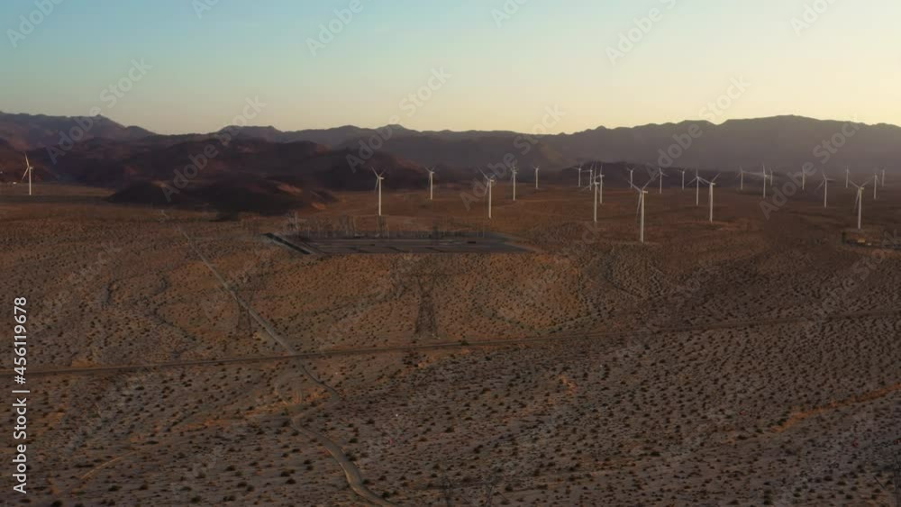 Car drives on desert road with windmill farm in distance. Birdseye view. Car drives on desert road with windmill farm in distance. Birdseye view.