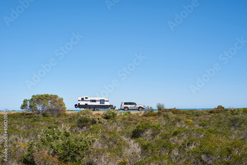 SUV towing a caravan along a coastal road in Western Australia under blue skies, with motion blur. photo