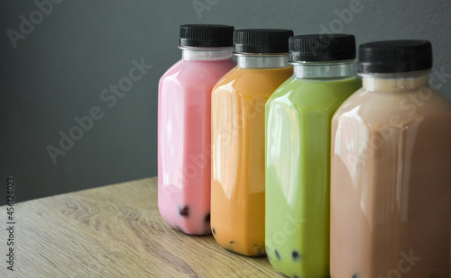 A row of various bobble tea in a plastic bottles on wooden table with black color background, copy space