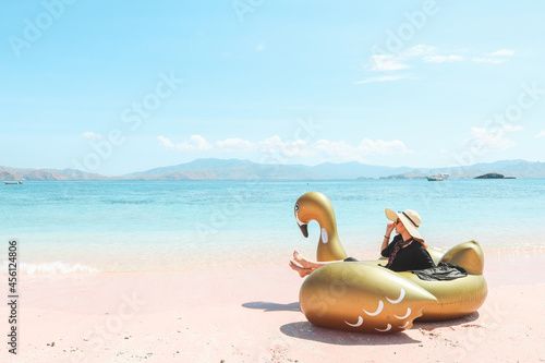 A girl in summer hat sitting on inflatable swan while enjoying sea view in pink sandy beach