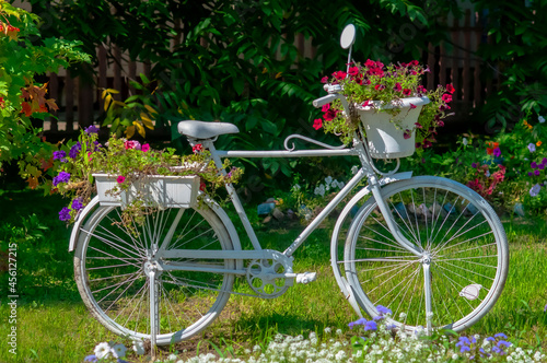 A white bicycle decorated with fresh flowers stands next to a red rowan bush. Beginning of autumn. Selective focus.