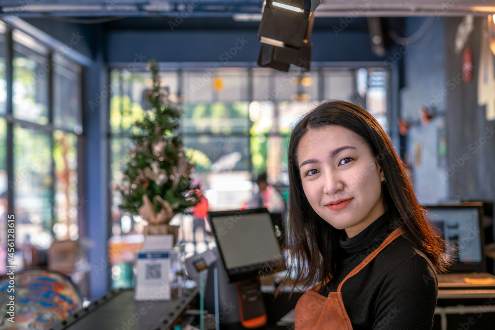 Portrait of confident Asian young adult owner gen z young woman at a counter bar in coffee shop cafe. She is wearing an apron looking at the camera and smiling. Hospitality and welcome concept Portrait of confident Asian young adult owner gen z young woman at a counter bar in coffee shop cafe. She is wearing an apron looking at the camera and smiling. Hospitality and welcome concept