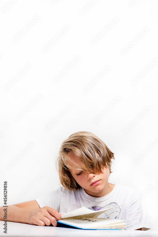 stylish boy reads an interesting book at his desk against a white wall background, back to school, vertical. stylish boy reads an interesting book at his desk against a white wall background, back to school, vertical.