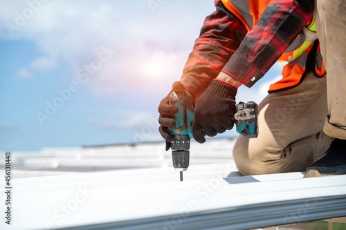 Roofer worker in protective uniform wear and gloves, using air or pneumatic nail gun and installing metal roof on top of the new roof,Concept of residential building under construction.