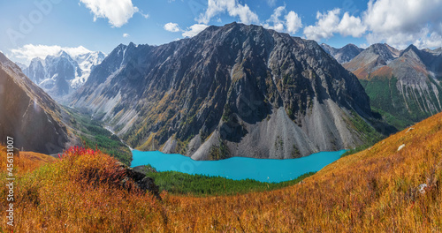 Panoramic autumn view to mountain lake on background of mountains. Atmospheric golden landscape with lake in high mountain valley.