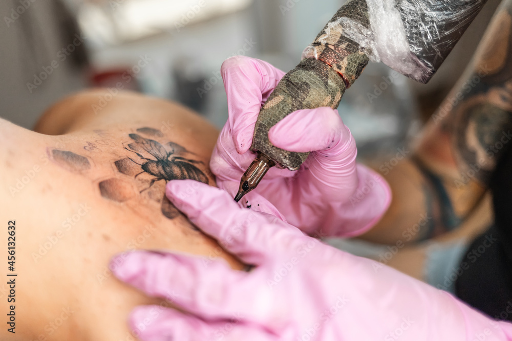 Obraz premium Modern youth culture. Close up of hands in pink latex gloves makes a tattoo design at client's back. Concept of world tattoo day