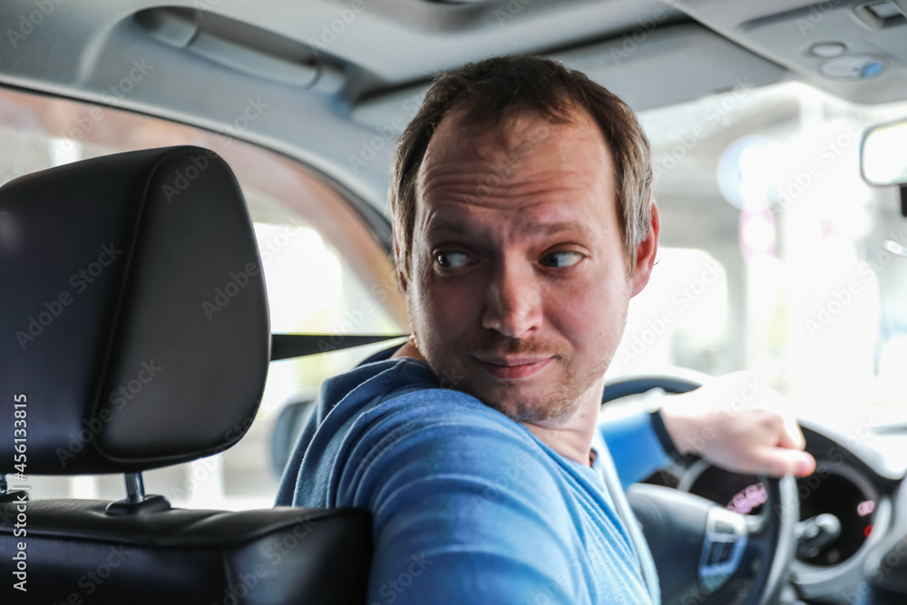 Obraz premium Blur image of the driver is driving a car. Blur photo from the salon of a man with a beard running a vehicle. A man looks away, while parking, a hand on the steering wheel.
