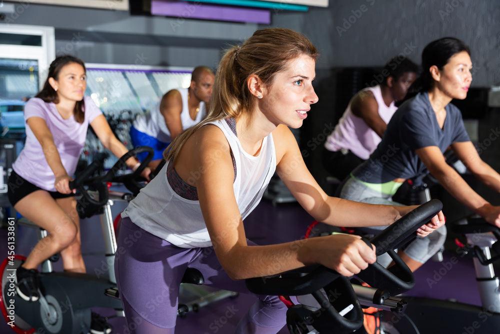Fototapeta premium Portrait of sporty young adult woman doing cardio workout cycling bike