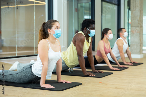 Multiethnic group of young adult people in protective face masks practicing pilates together at fitness center during coronavirus pandemic