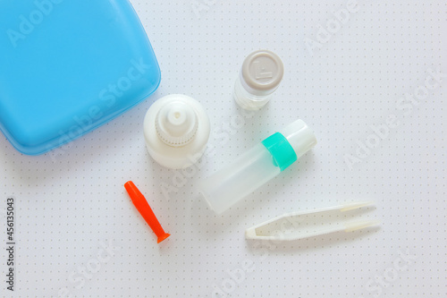 Rigid contact lens  on light background with holder, liquid, container, cleanser, tweezers and sucker
