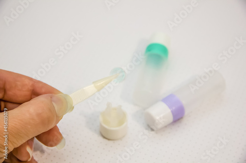 Rigid contact lens in hands on light background with holder, liquid, container, cleanser, tweezers and sucker