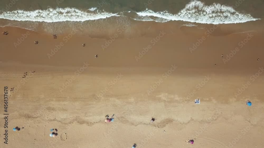 Tourists Enjoying Summer Heat At Sandy Beach By The Lighthouse. Playa Faro de Trafalgar In Cadiz, Spain. aerial top-down Tourists Enjoying Summer Heat At Sandy Beach By The Lighthouse. Playa Faro de Trafalgar In Cadiz, Spain. aerial top-down