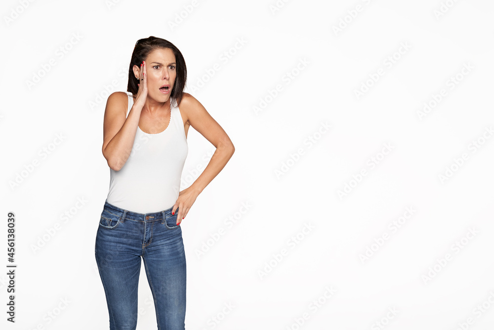 Beautiful woman surprised on isolated soft background. Woman in denim pants and white tank top. Beautiful woman surprised on isolated soft background. Woman in denim pants and white tank top.