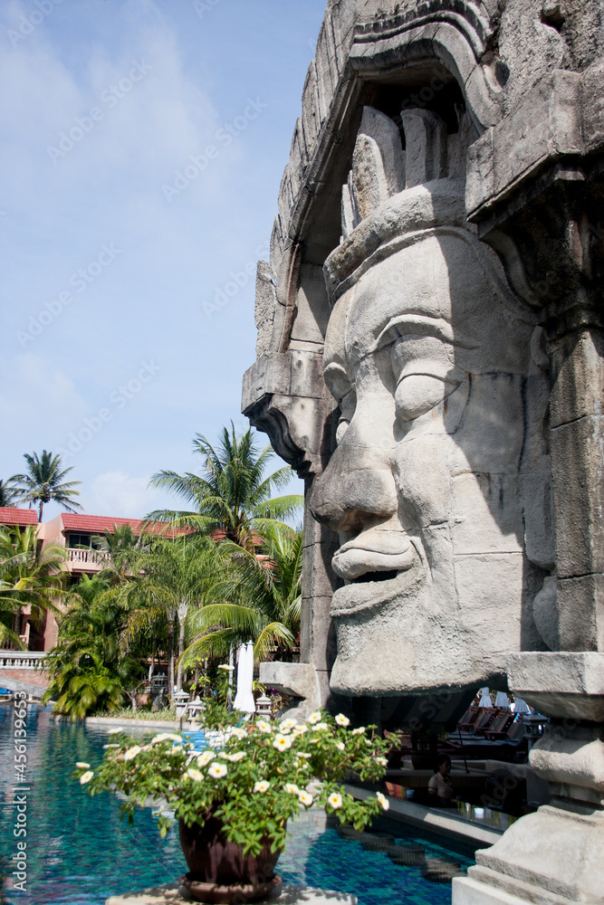the head of a Thai god on the background of a pool and palm trees
