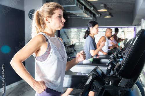 Portrait of sporty young adult woman doing cardio workout running on treadmill at fitness center