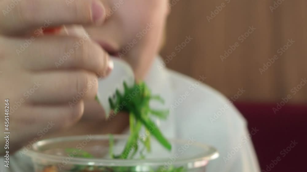 A boy in a cafe with tablet eats a salad of fresh vegetables, with salad and seaweed. vegetarianism. Healthy food, diet. healthy salad on a white platter, on a straw table, top view. Vegetarian food. A boy in a cafe with tablet eats a salad of fresh vegetables, with salad and seaweed. vegetarianism. Healthy food, diet. healthy salad on a white platter, on a straw table, top view. Vegetarian food.