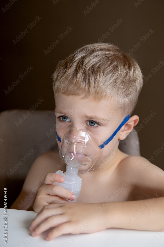 A sad little boy does inhalations with a nebulizer at home, he is sick. Help at home with cough, asthma. Concept health