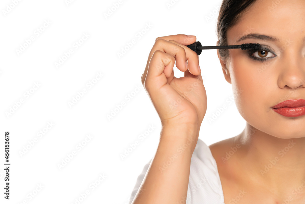 a half portrait of a young woman applies mascara