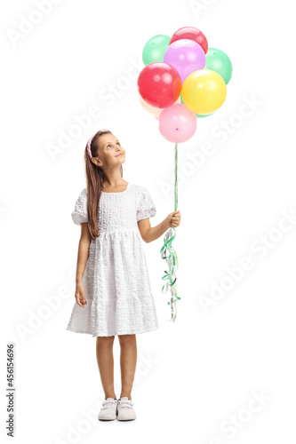 Full length portrait of a girl in a white dress holding a bunch of balloons and looking up