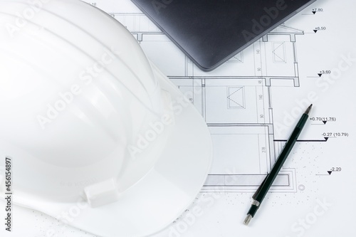 A pen, a white safety helmet and a laptop on the architectural plan