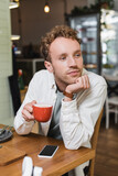 pensive man holding cup of cappuccino and looking away in cafe
