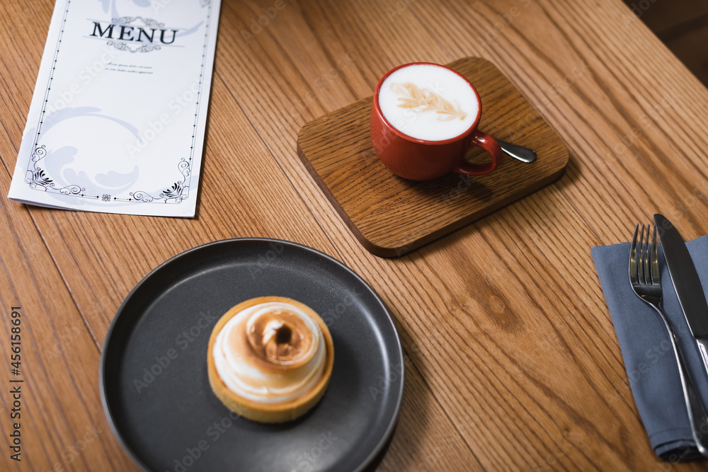 high angle view of lemon tart and cappuccino near menu on table high angle view of lemon tart and cappuccino near menu on table