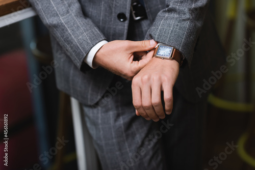 cropped view of young businessman in formal wear adjusting wristwatch