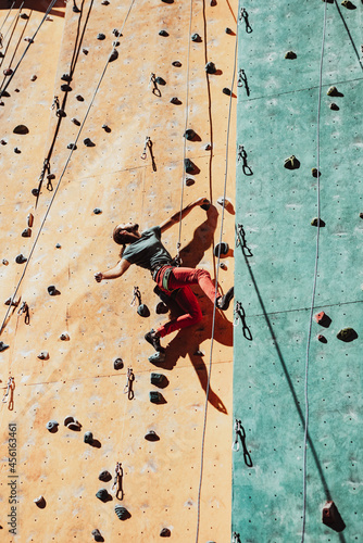 One Caucasian man professional rock climber workouts on climbing wall at training center in sunny day, outdoors. Concept of healthy lifestyle, power, strength, motion.