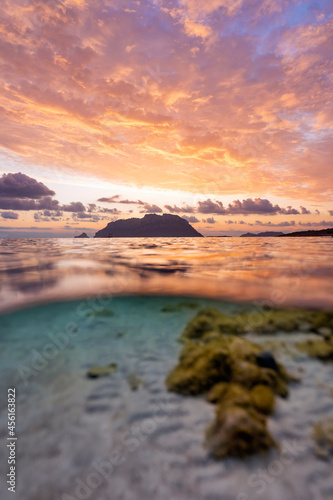  Selective focus  Split shot  over under water surface. Defocused waves in the foreground with Tavolara Island on the surface during a dramatic sunrise. Porto Istana  Sardinia  Italy.