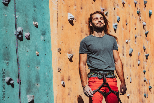 Portrait of Caucasian man professional rock climber standing at front of climbing wall at training center in sunny day, outdoors. Concept of healthy lifestyle, sport, motion.