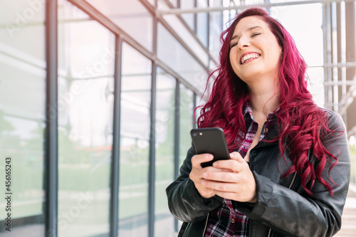 Pink hair woman using smart phone in the city and laughing