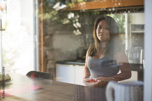 Portrait of Japanese woman in kitchen. Beautiful Asian girl standing at window holding plate with cherry tomatoes. Food, household concept © KAMPUS