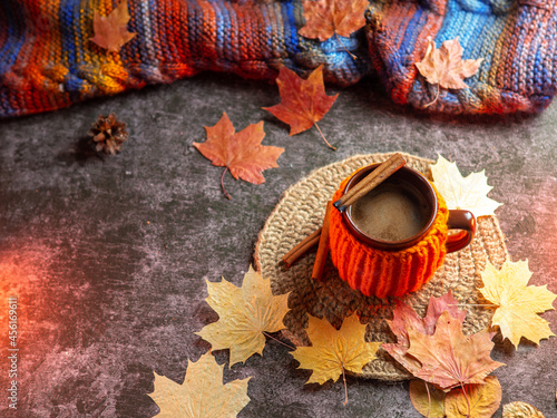 A hot cup of coffee in an orange jacket and a knitted autumn colorful scarf, autumn maple leaves