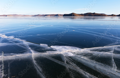 Unusual winter landscape with a cracks in the blue smooth surface of the ice on frozen Lake Baikal at sunny frosty day. Natural winter background