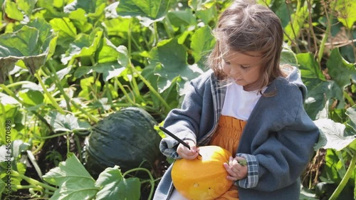 A child paints a scary face on a pumpkin for Halloween. Children are preparing for the feast of all saints.