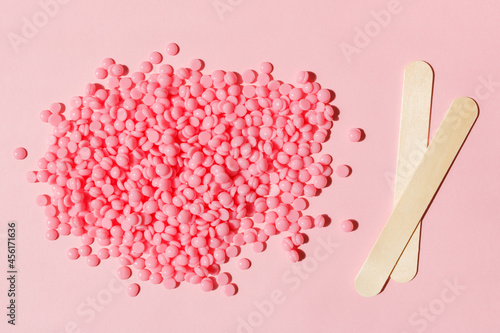 Beautiful pink depilatory wax granules and wooden spatulas on a pink background. Epilation, depilation, unwanted hair removal. Top view.