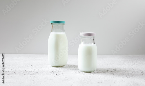 Two glass reusable bottles of fresh organic milk or dairy product on a white wooden table