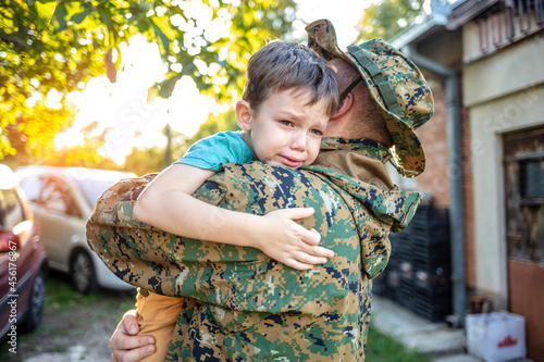 Fototapeta An emotional military father, dressed in camouflage, holds his young son in arms in greeting after returning home from a tour of duty overseas