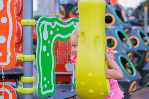 Wallpaper Mural girl 6-7 years old, cute blonde, with a sly look, on the playground in the theme park, looking out from behind a swing, portrait of a child Torontodigital.ca