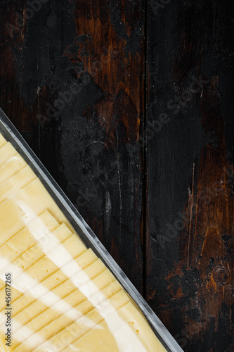 Slices of yellow cheese in sealed pack, on dark wooden background with copy space for text