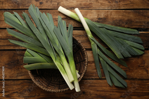 Fresh raw leeks and wicker bowl on wooden table, flat lay