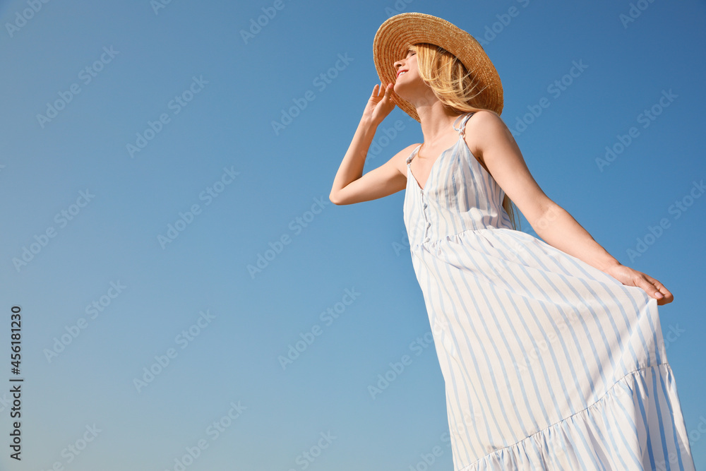 Beautiful woman with straw hat against blue sky on sunny day, space for text