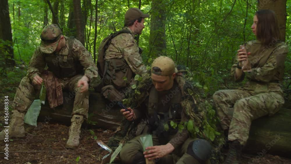 Soldier opening ration meal with butterfly knife, asking companion to hand over it to gunner while preparing MRE pack for eating during halt in forest. Guardsman taking blade, cleaning and close it up Soldier opening ration meal with butterfly knife, asking companion to hand over it to gunner while preparing MRE pack for eating during halt in forest. Guardsman taking blade, cleaning and close it up