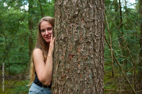 A blonde Caucasian lady with long hair making smiling next to a tree in the forest © Érik Glez.