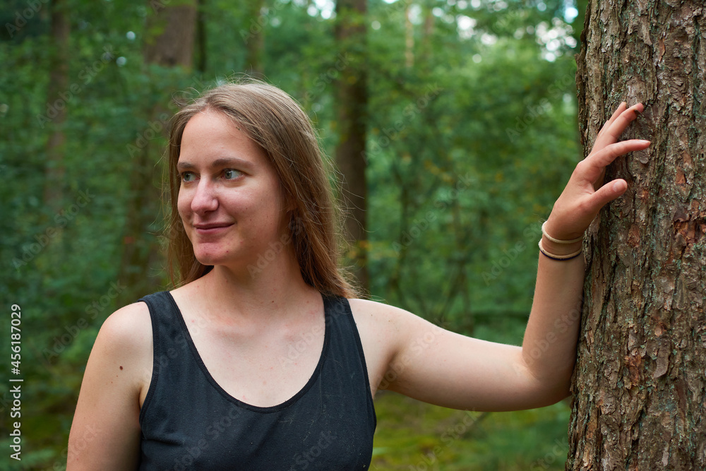 A blonde Caucasian lady with long hair posing next to a tree trunk in the forest A blonde Caucasian lady with long hair posing next to a tree trunk in the forest