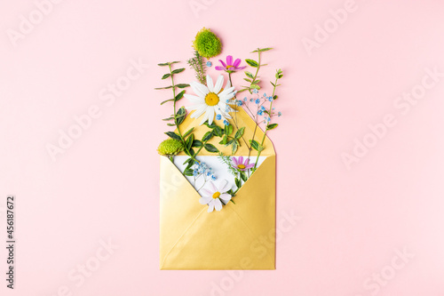 Golden envelope with beautiful spring garden flowers on pink background