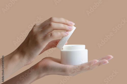 Women's hands open mock-up of jar of cream, showing contents on beige background. Concept of beauty industry, body care