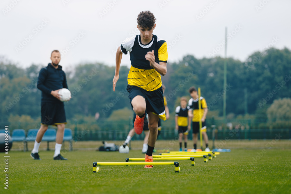 Obraz premium Junior soccer player running fast and ladder skipping. Boys practice football witch young coach. Teenagers on soccer training camp. Youth athletes improving soccer skills on outdoor training