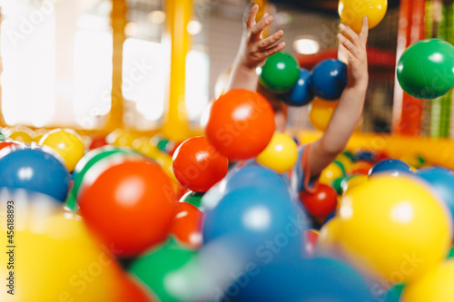 Happy child playing at balls pool playground. Kid playing with multi coloured plastic balls in big dry paddling pool in playing centre. School boy having fun in indoor park playground photo